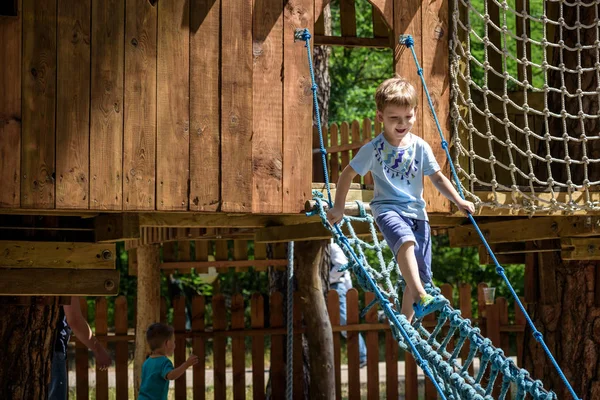 Der kleine Kletterer nimmt die Hängebrücke. Junge hat Spaß, Kind klettert an sonnigem, warmen Sommertag — Stockfoto