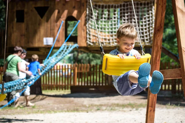 Sommer, Kindheit, Freizeit, Freundschaft und Menschen-Konzept - fröhlicher kleiner Junge schaukelt auf Schaukel auf Kinderspielplatz — Stockfoto