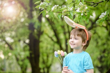 Küçük çocuk bahar bahçesinde paskalya yumurtası arıyor. Şirin. 