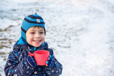 Sıcak çikolata veya çocuk yumruk buğulaması Kupası olan küçük şirin çocuk çocuk. Mutlu çocuk oyun kış orman açık havada