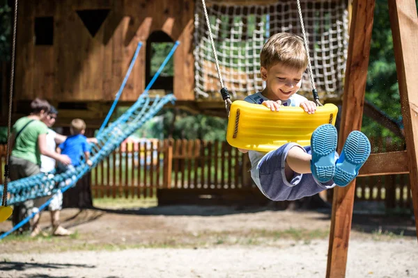 Summer, childhood, leisure, friendship and people concept - happy little boy swinging on swing at children playground — Stock Photo, Image