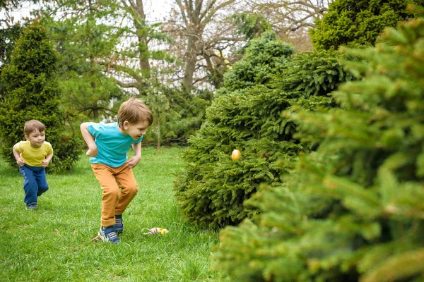 Los niños en la búsqueda de huevos de Pascua en el floreciente jardín de primavera. Niños en busca de huevos de colores en el prado de flores. niño pequeño y su hermano amigo niño jugar al aire libre — Foto de Stock