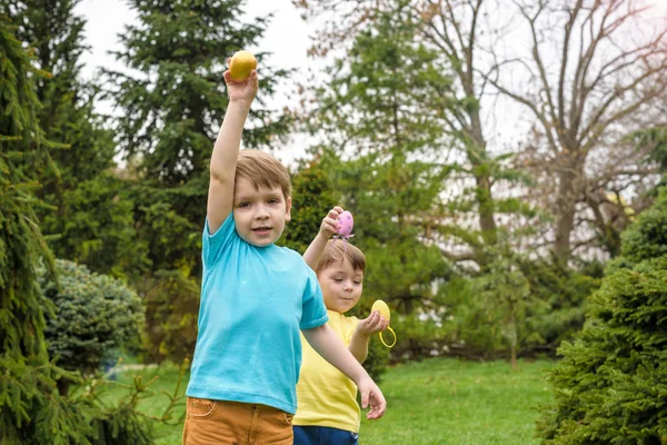 Los niños en la búsqueda de huevos de Pascua en el floreciente jardín de primavera. Niños en busca de huevos de colores en el prado de flores. niño pequeño y su hermano amigo niño jugar al aire libre — Foto de Stock