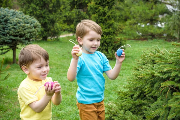 Los niños en la búsqueda de huevos de Pascua en el floreciente jardín de primavera. Niños en busca de huevos de colores en el prado de flores. niño pequeño y su hermano amigo niño jugar al aire libre — Foto de Stock