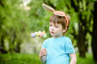Küçük çocuk bahar bahçesinde paskalya yumurtası arıyor. Şirin. 