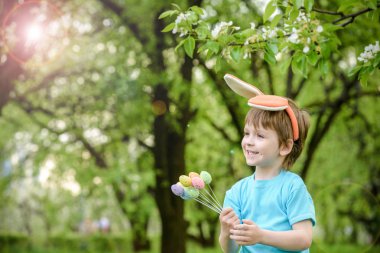 Küçük çocuk bahar bahçesinde paskalya yumurtası arıyor. Şirin. 