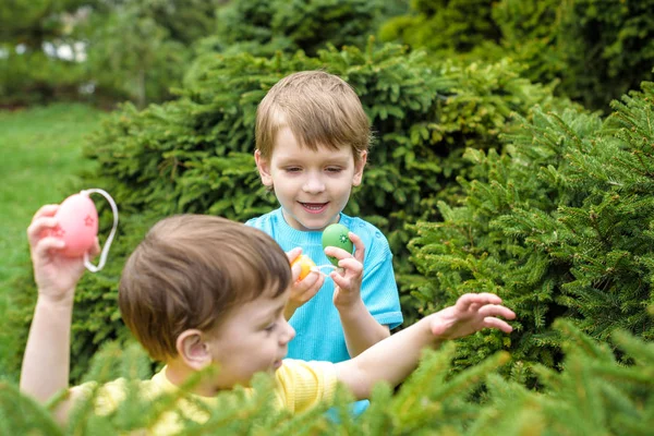 Los niños en la búsqueda de huevos de Pascua en el floreciente jardín de primavera. Niños en busca de huevos de colores en el prado de flores. niño pequeño y su hermano amigo niño jugar al aire libre — Foto de Stock