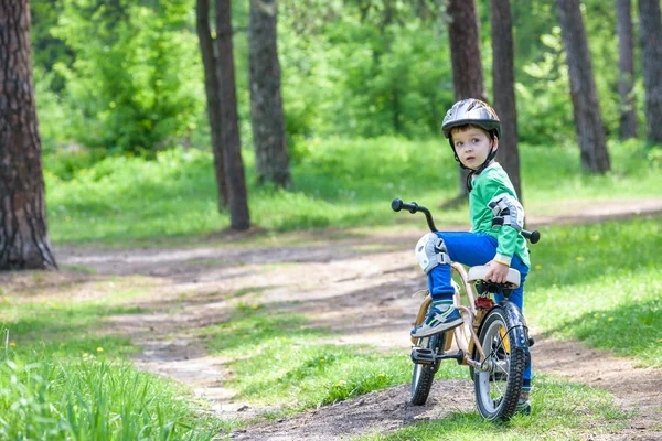 Счастливый симпатичный мальчик веселится на своем первом велосипеде в солнечное лето — стоковое фото