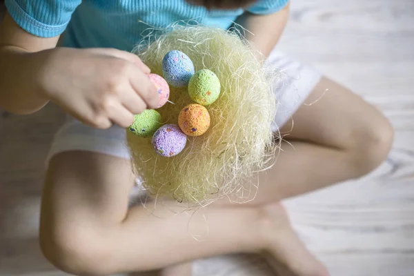 Milý chlapeček držící hnízdo s barevné velikonoční vajíčka doma na velikonoční den. Oslava Velikonoc na jaro. Malování vajíček — Stock fotografie