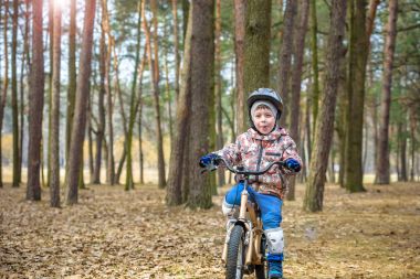 Güzel sonbahar gününde bir bisiklet ile sonbahar ormandaki eğleniyor 3 veya 5 yıllık mutlu bir çocukluk oğlan. Etkin alt giyen Bisiklet kask. Güvenlik, spor, eğlence çocuk kavramı ile.