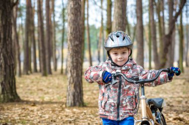 Güzel sonbahar gününde bir bisiklet ile sonbahar ormandaki eğleniyor 3 veya 5 yıllık mutlu bir çocukluk oğlan. Etkin alt giyen Bisiklet kask. Güvenlik, spor, eğlence çocuk kavramı ile.