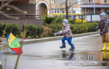 İki küçük çocuğu, bir su birikintisi üzerinde bodur küçük şemsiye ile