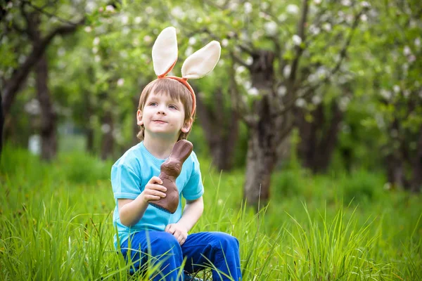 Menino pequeno feliz comendo chocolate e vestindo pão de Páscoa — Fotografia de Stock