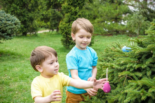 Los niños en la búsqueda de huevos de Pascua en el floreciente jardín de primavera. Niños en busca de huevos de colores en el prado de flores. niño pequeño y su hermano amigo niño jugar al aire libre — Foto de Stock