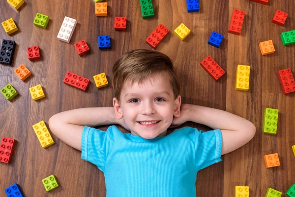 Pequeño niño caucásico jugando con un montón de bloques de plástico de colores en el interior. Niño niño vistiendo camisa y divertirse creando — Foto de Stock