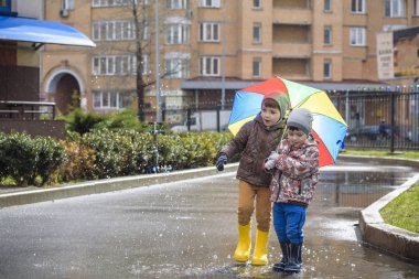 İki küçük çocuğu, bir su birikintisi üzerinde bodur küçük şemsiye ile