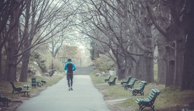 Arkadan görüntüleyin. Bahar Parkı doğada çalıştıran ve müzik dinlerken kulaklık olan genç adam. Yaşam sağlık kavramı