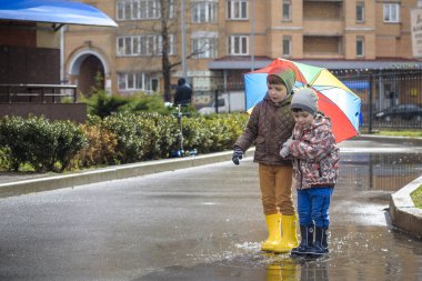 İki küçük çocuğu, bir su birikintisi üzerinde bodur küçük şemsiye ile