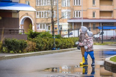 İki küçük çocuğu, bir su birikintisi üzerinde bodur küçük şemsiye ile