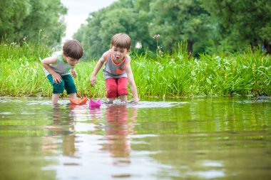 İki küçük kardeş ile oynarken kağıt tekneler bir nehir tarafından üzerinde sıcak ve güneşli yaz gün.