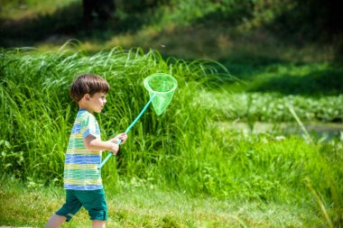Kepçe-net çayır ile sıcak ve güneşli yaz veya bahar günü oynayan sevimli beyaz çocuk.