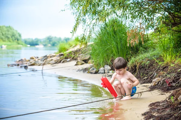 Niño jugando con el juguete del barco en el mar. Niño os de vacaciones en verano en la playa de vacaciones — Foto de Stock