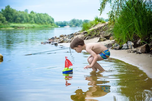 Niño jugando con el juguete del barco en el mar. Niño os de vacaciones en verano en la playa de vacaciones — Foto de Stock