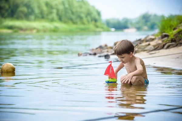 Niño jugando con el juguete del barco en el mar. Niño os de vacaciones en verano en la playa de vacaciones — Foto de Stock