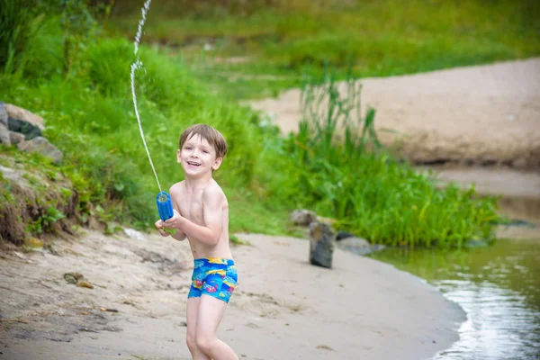 Retrato de niño caucásico en sombrero de paja jugando juguetes y bomba de agua en la playa . — Foto de Stock