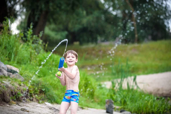 Retrato de niño caucásico en sombrero de paja jugando juguetes y bomba de agua en la playa . — Foto de Stock