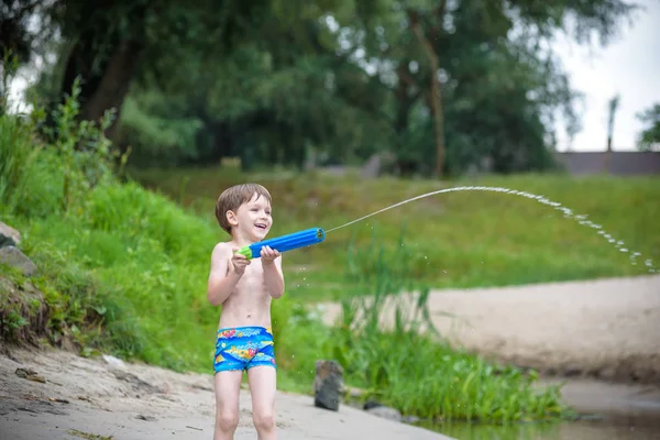 Retrato de niño caucásico en sombrero de paja jugando juguetes y bomba de agua en la playa . — Foto de Stock