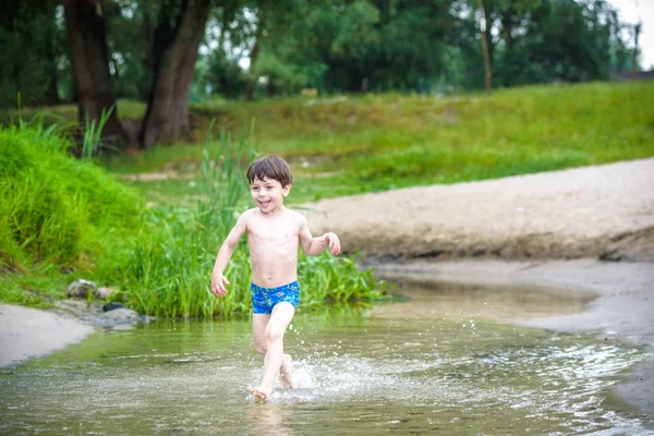 Niño feliz divirtiéndose y corriendo en el agua en el río a la hora del día de verano, estilo de vida veraniego al aire libre, concepto de fin de semana familiar amigable, estilo de vida activo saludable — Foto de Stock