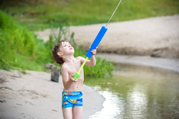 Retrato de niño caucásico en sombrero de paja jugando juguetes y bomba de agua en la playa . — Foto de Stock