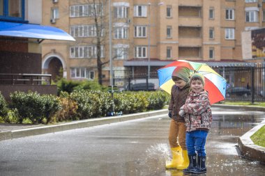 İki küçük çocuğu, bir su birikintisi üzerinde bodur küçük şemsiye ile