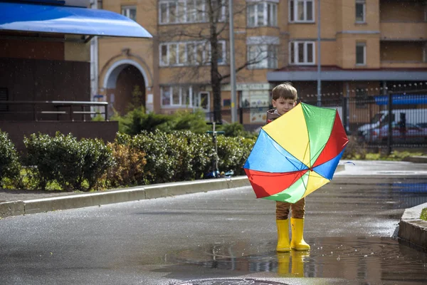 Un niño jugando en el parque de verano lluvioso. Niño con rai colorido — Foto de Stock