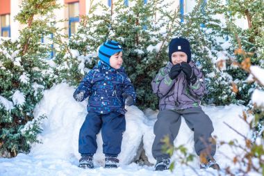 İki küçük çocuklar renkli giysiler açık havada kar yağışı sırasında oynayan çocuk. Kışın soğuk günlerinde çocuklu etkin boş. Mutlu kardeşler ve eğleniyor İkizler kar