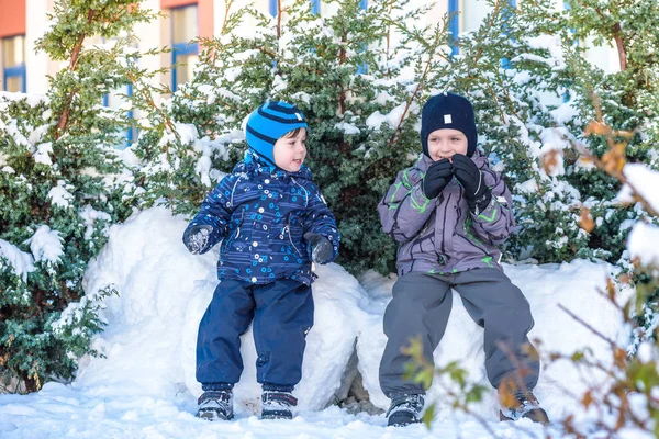 İki küçük çocuklar renkli giysiler açık havada kar yağışı sırasında oynayan çocuk. Kışın soğuk günlerinde çocuklu etkin boş. Mutlu kardeşler ve eğleniyor İkizler kar