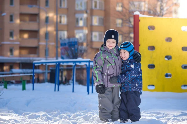 Two little kid boys in colorful clothes playing outdoors during snowfall. Active leisure with children in winter on cold days. Happy siblings and twins having fun snow — Stock Photo, Image