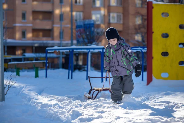 행복 한 아이 겨울 도시에 야외에서 걷고 그의 썰매를 끌. 자식 웃 고 데 재미. — 스톡 사진