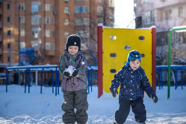 Two little kid boys in colorful clothes playing outdoors during snowfall. Active leisure with children in winter on cold days. Happy siblings and twins having fun snow — Stock Photo, Image