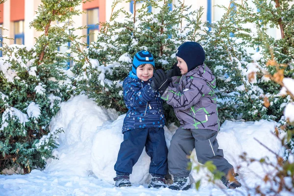 Due ragazzini in abiti colorati che giocano all'aperto durante le nevicate. Tempo libero attivo con i bambini in inverno nelle giornate fredde. Buoni fratelli e gemelli che si divertono con la neve — Foto Stock