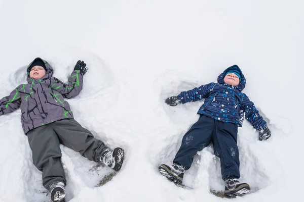 Dwoje rodzeństwa mały dzieciak chłopców w kolorowe zimowe ubrania, co Anioł śniegu, ustanawiające. Na zewnątrz aktywny wypoczynek z dziećmi w Szczęśliwy braci — Zdjęcie stockowe