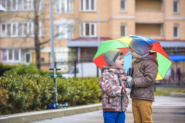 Two little boys, squat on a puddle, with little umbrellas — Stock Photo, Image