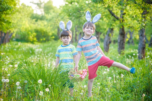 Děti na velikonoční hon na vajíčka v kvetoucí jarní zahradě. Děti hledají barevná vejce na květinové louce. Batole chlapec a jeho bratr přítel chlapec hrát venku — Stock fotografie