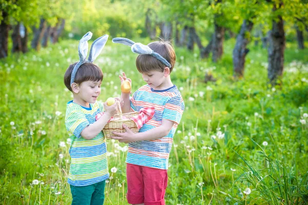 Kids on Easter egg hunt in blooming spring garden. Children searching for colorful eggs in flower meadow. Toddler boy and his brother friend kid boy play outdoors
