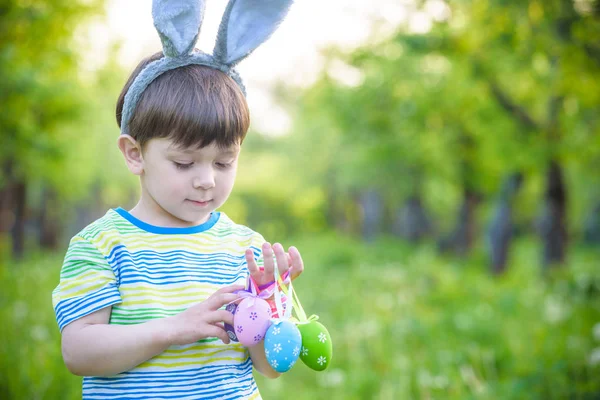 Dzieciak na Easter egg hunt w kwitnące wiosną ogród. chłopiec, szukając kolorowych jaj w łące kwiat — Zdjęcie stockowe