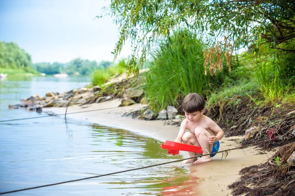 Niño jugando con el juguete del barco en el mar. Niño os de vacaciones en verano en la playa de vacaciones — Foto de Stock