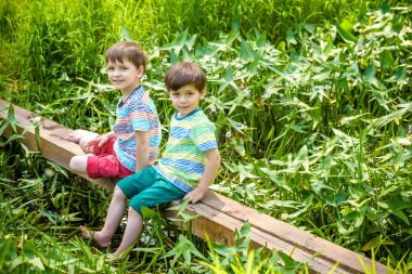 İki sevimli küçük çocuklar bir ahşap köprü üzerinde oturan
