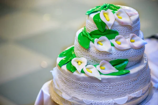 Pastel de boda de tres niveles está decorado con flores y puestos en la mesa junto a un plato y cubiertos —  Fotos de Stock