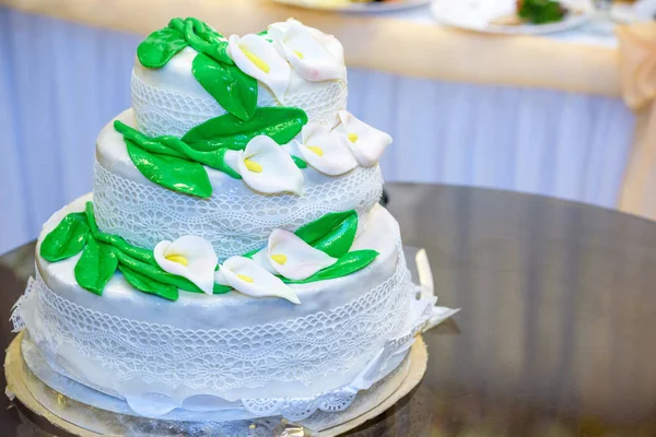 3 poziomowym tort weselny jest ozdobiony kwiatami i stoi na stoliku obok talerz i sztućce — Zdjęcie stockowe